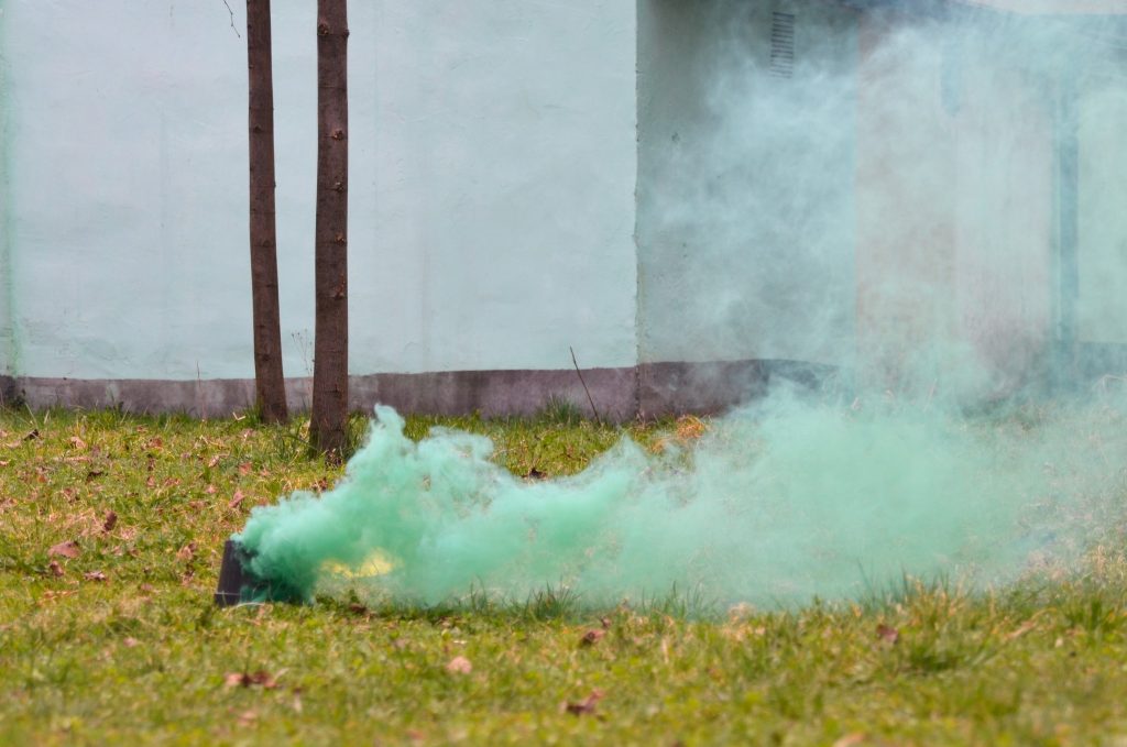 Świeca dymna generująca jaskrawozielony dym z puszki leżącej na trawie.