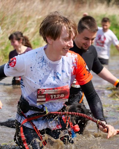 Ujęcie w ruchu z biegu Hard Dog Race - przeprawa przez rzekę, pływające psy, uśmiech na twarzach opiekunów.